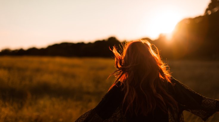 Woman running through field at sunset